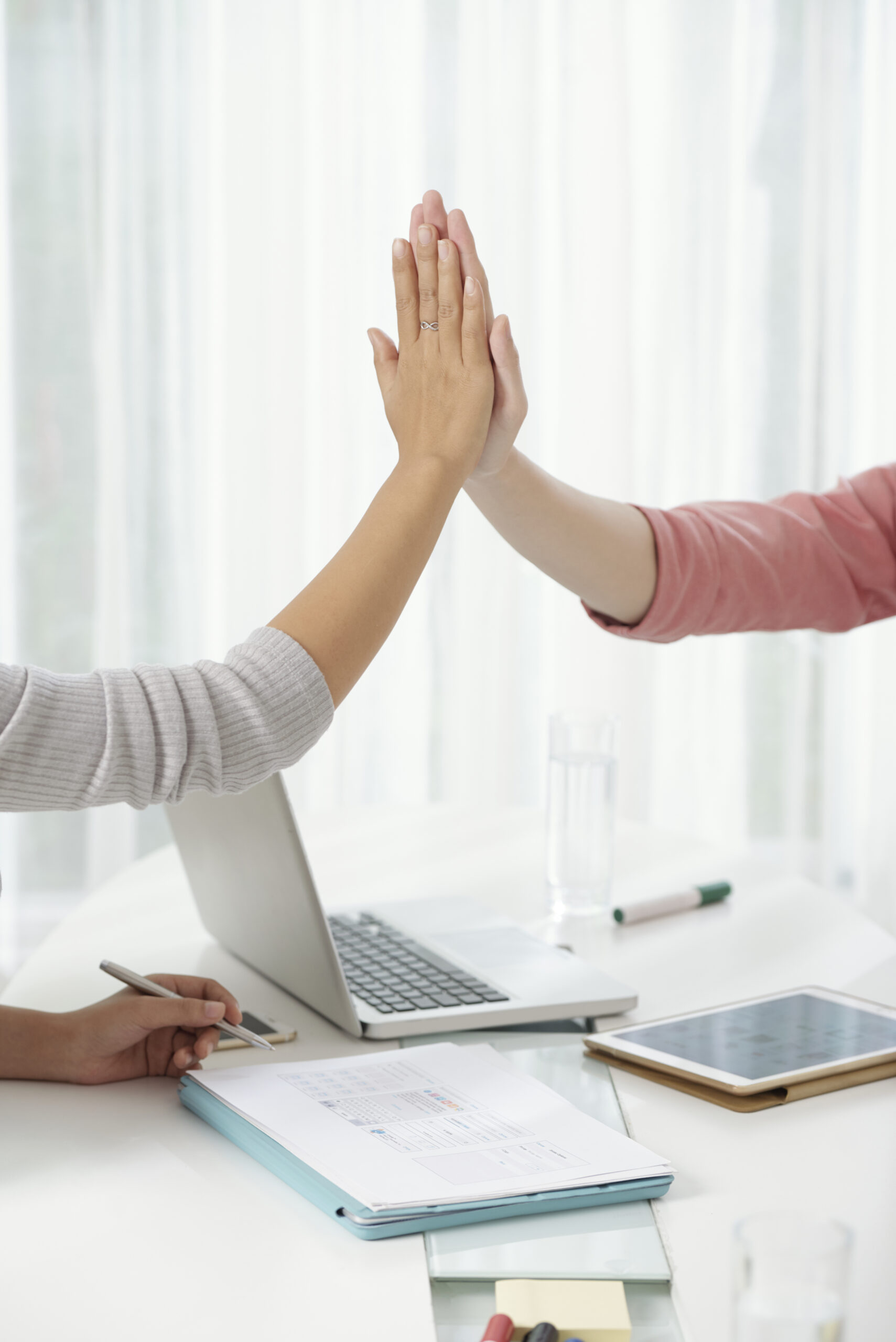 Crop hands of modern coworkers giving high five above working table with gadgets